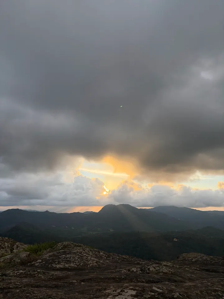 Evening sun breaking through dark clouds over the hills seen from Bandekallu Gudda